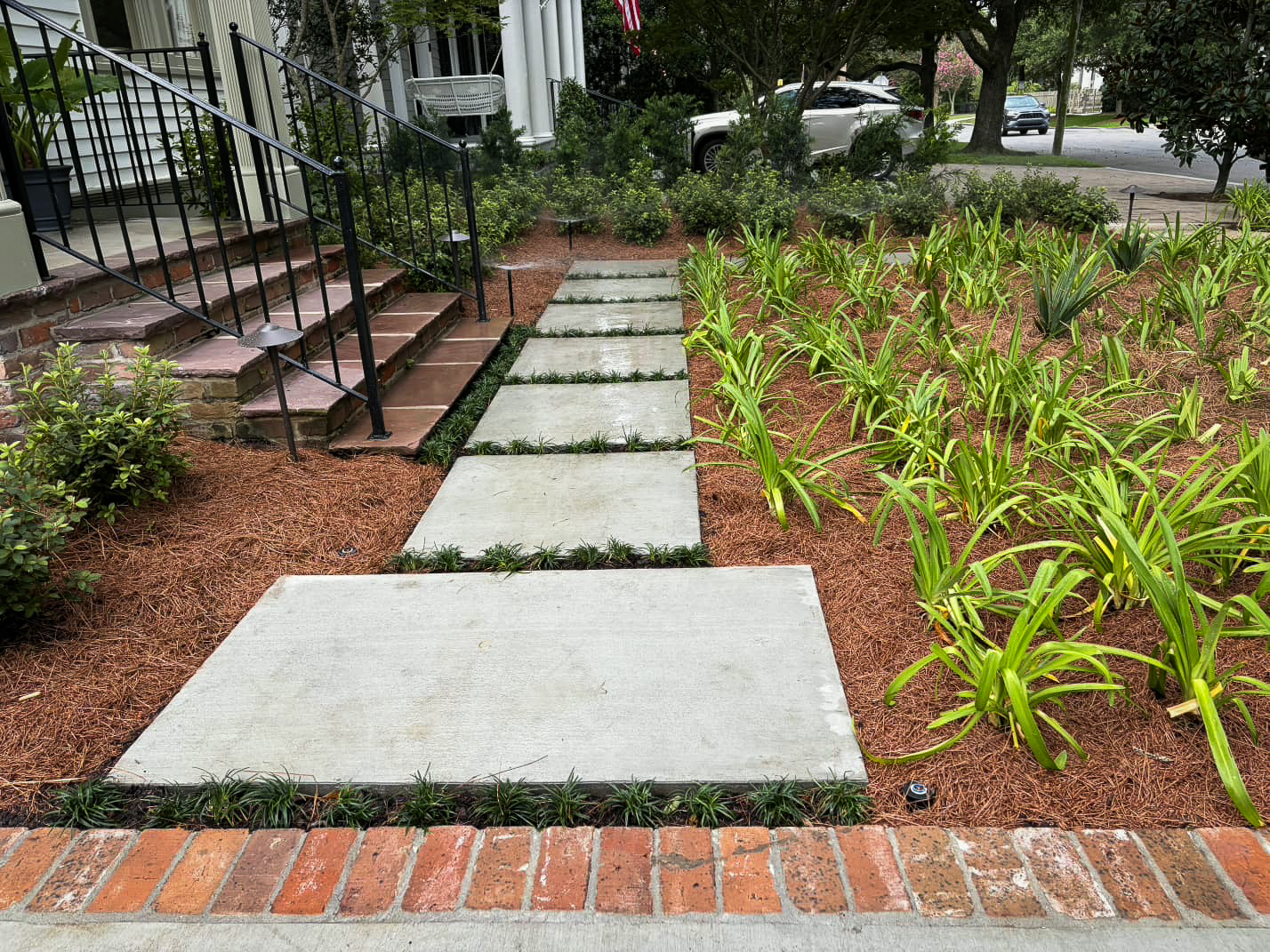 State Street front entry path with oversized concrete pavers, dwarf mondo grass joints, agapanthus, pine straw mulch, and low-voltage landscape lighting.