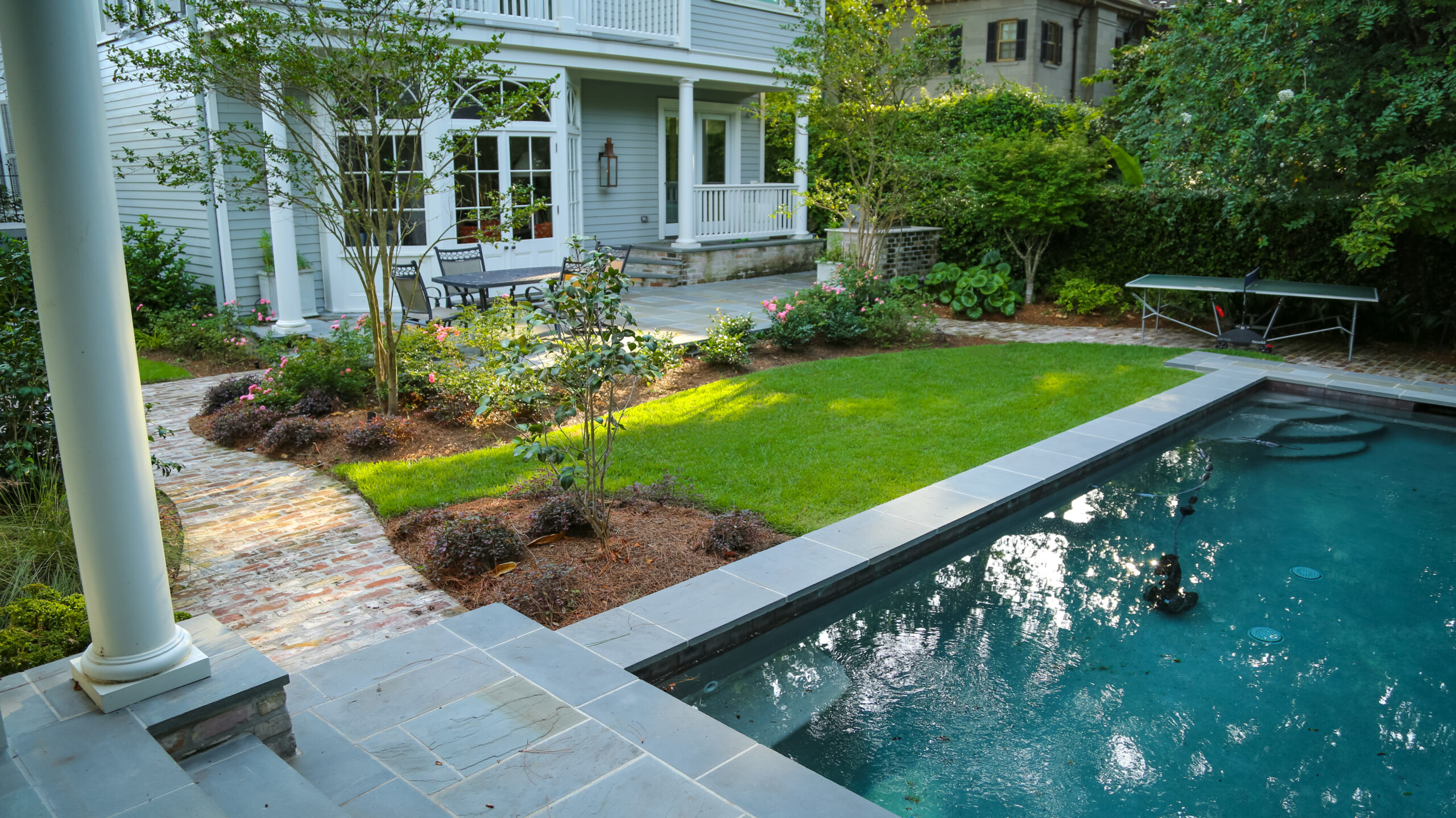 Swimming pool, lawn, brick paths, and layered planting in a Garden District landscape design