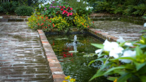 Brick-edged garden fountain with water lilies and seasonal flowers in a Garden District landscape