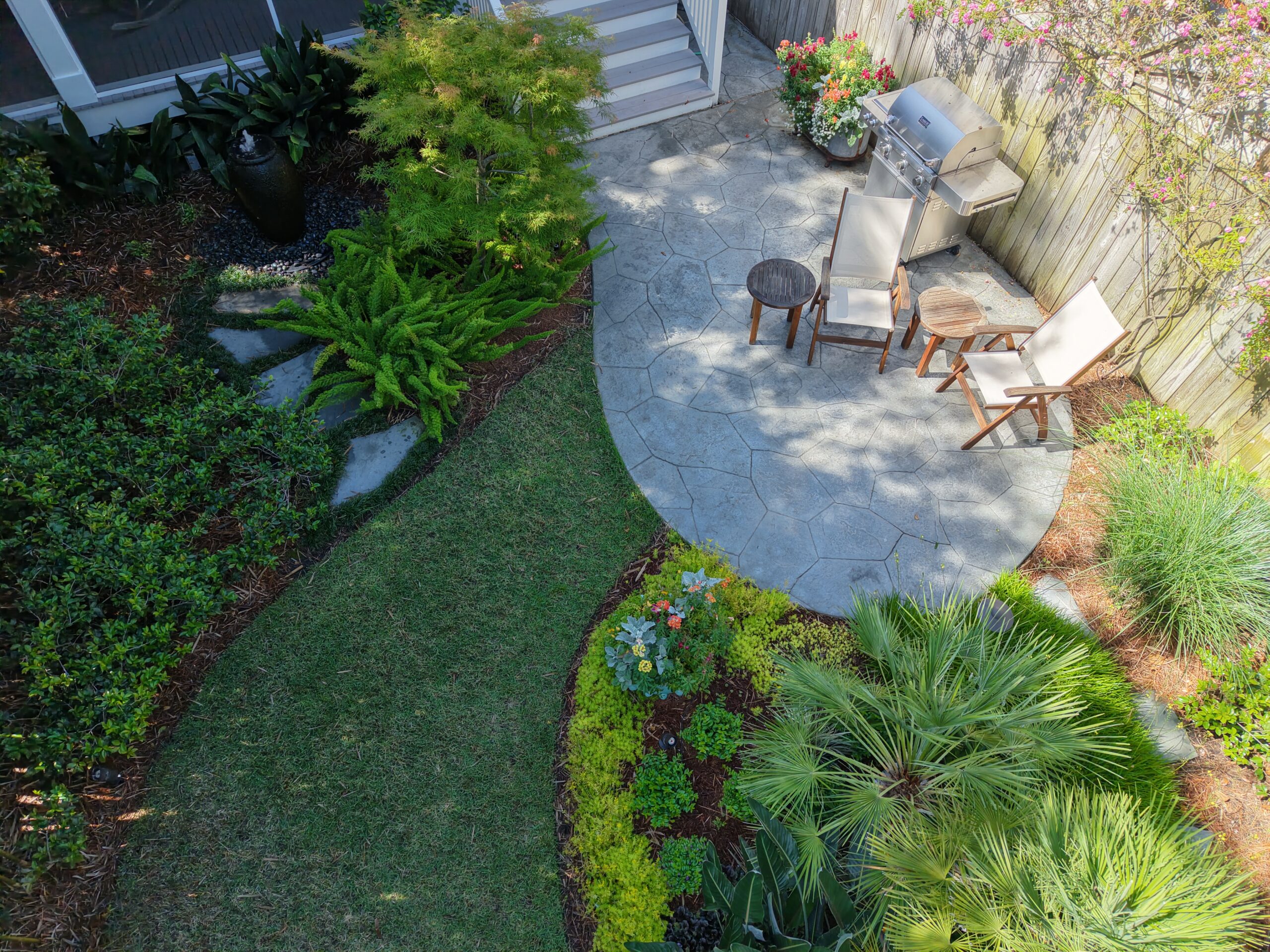 Aerial view of a curved lawn, stone patio, and layered planting in an Uptown New Orleans garden