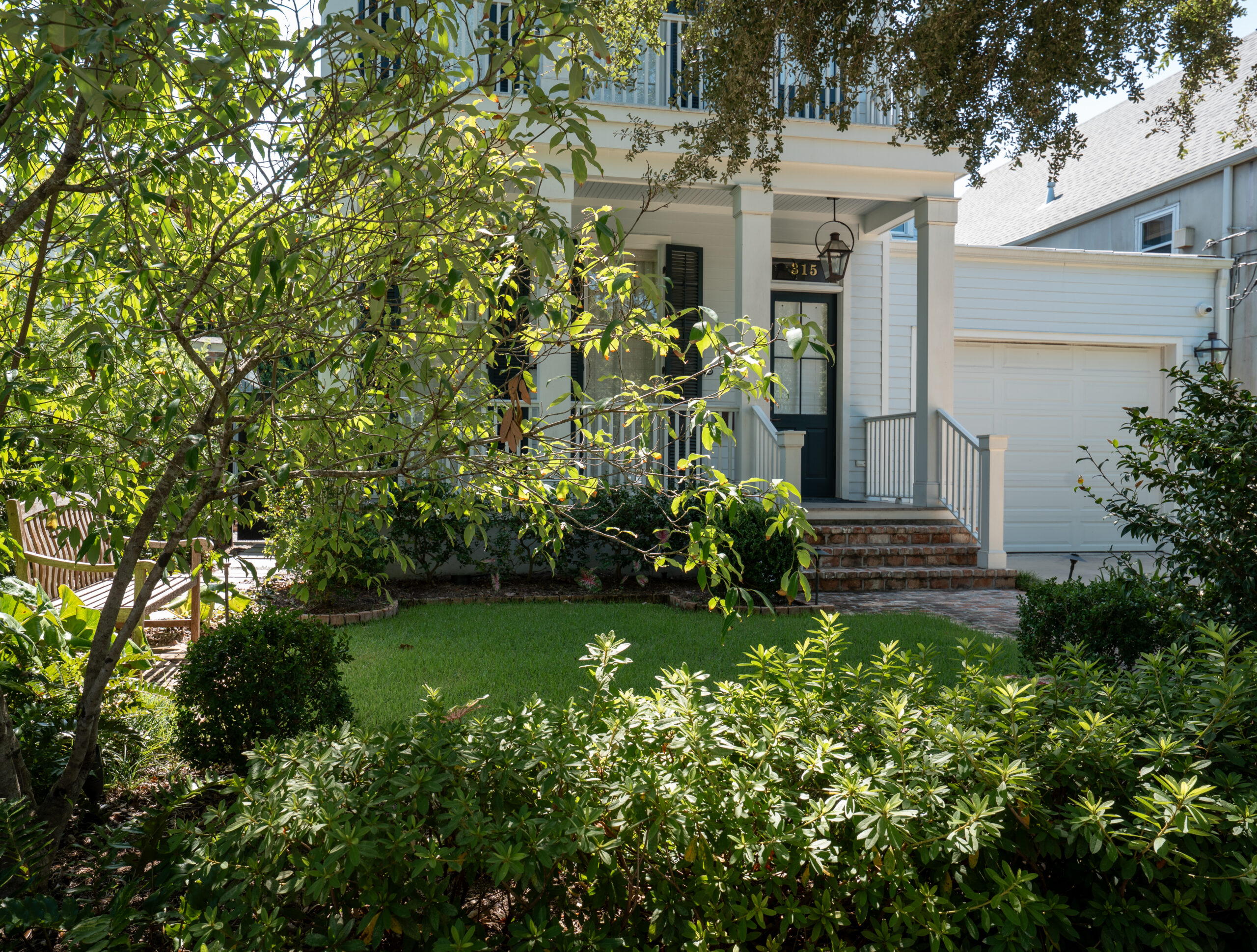 Maintained front garden with clipped hedges and layered plantings framing a New Orleans residence.