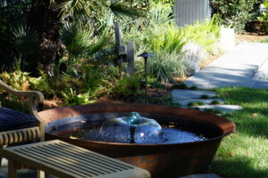 Round bubbling water feature surrounded by palms and tropical planting in an Uptown New Orleans garden