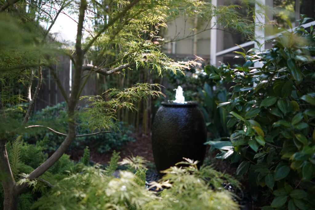 Traditional Uptown New Orleans home framed by established palms, flowering plants, and layered garden beds