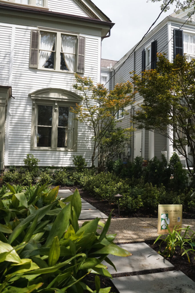 Traditional Uptown New Orleans side garden with a stepping-stone path, Japanese maples, layered evergreen plantings, and low-voltage landscape lighting.