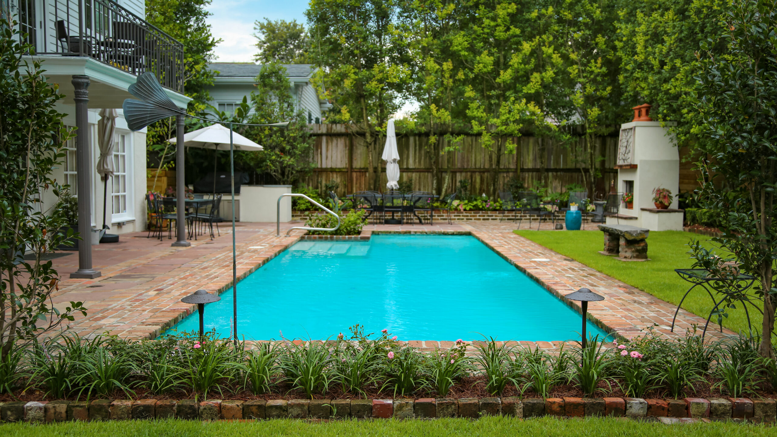 Rectangular swimming pool framed by brick paving and layered planting in an Uptown New Orleans garden