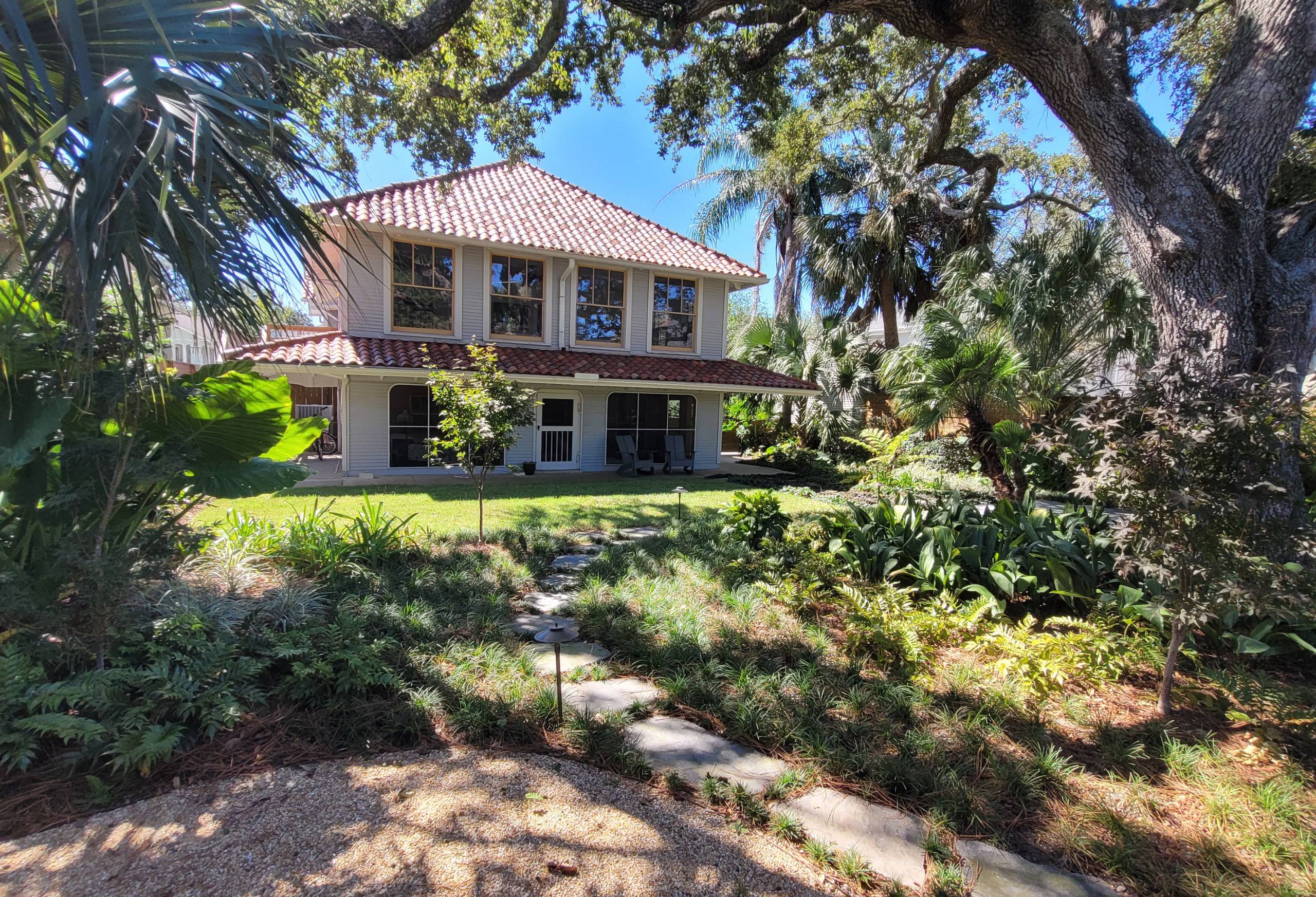 Lush Lakeview New Orleans backyard landscape with a stone path, shade garden plantings, palms, and mature live oak trees