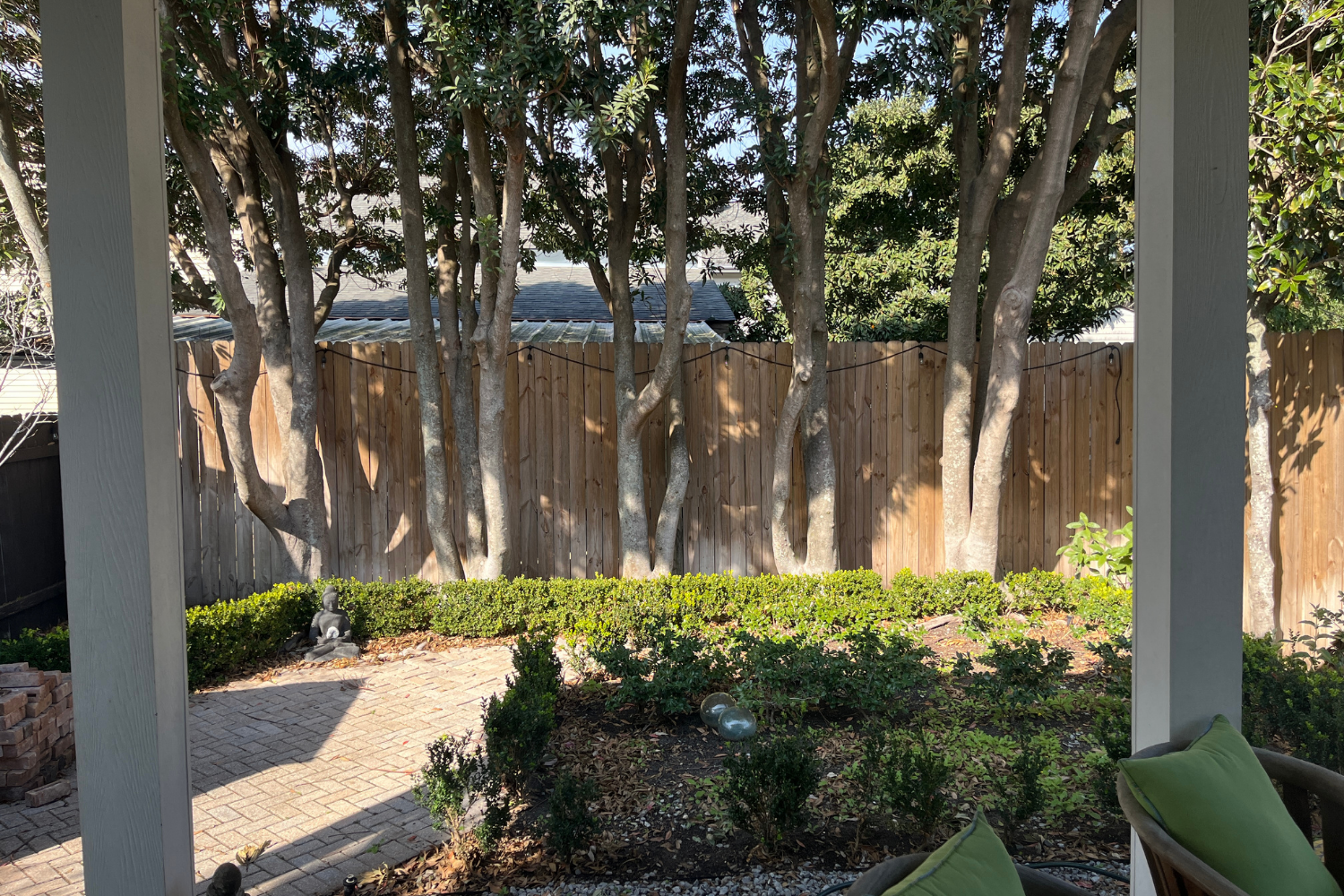 Existing garden bed with mature trees, low hedging, pavers, a gray shed, and a wood privacy fence before landscape installation.