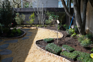 Landscape installation with an irregular flagstone path set in crushed brownstone, curved brick edging, and new planting beneath mature trees.