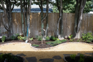 Curved crushed brownstone garden path with flagstone steppers, brick edging, and newly installed planting below mature trees