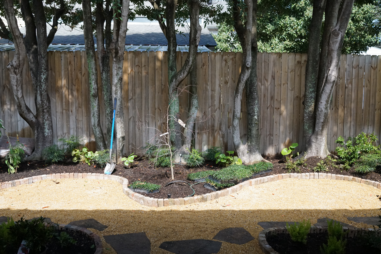 Curved crushed brownstone garden path with flagstone steppers, brick edging, and newly installed planting below mature trees