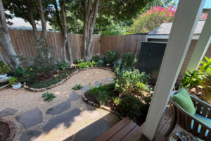 Curved crushed brownstone path with flagstone steppers, brick-edged planting beds, and mature trees at the Constance Street Garden in Uptown New Orleans