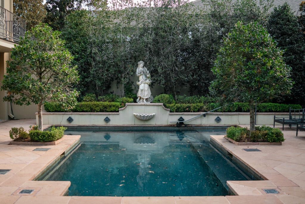 Formal New Orleans courtyard pool with a classical garden statue, clipped boxwood, and layered evergreen planting.