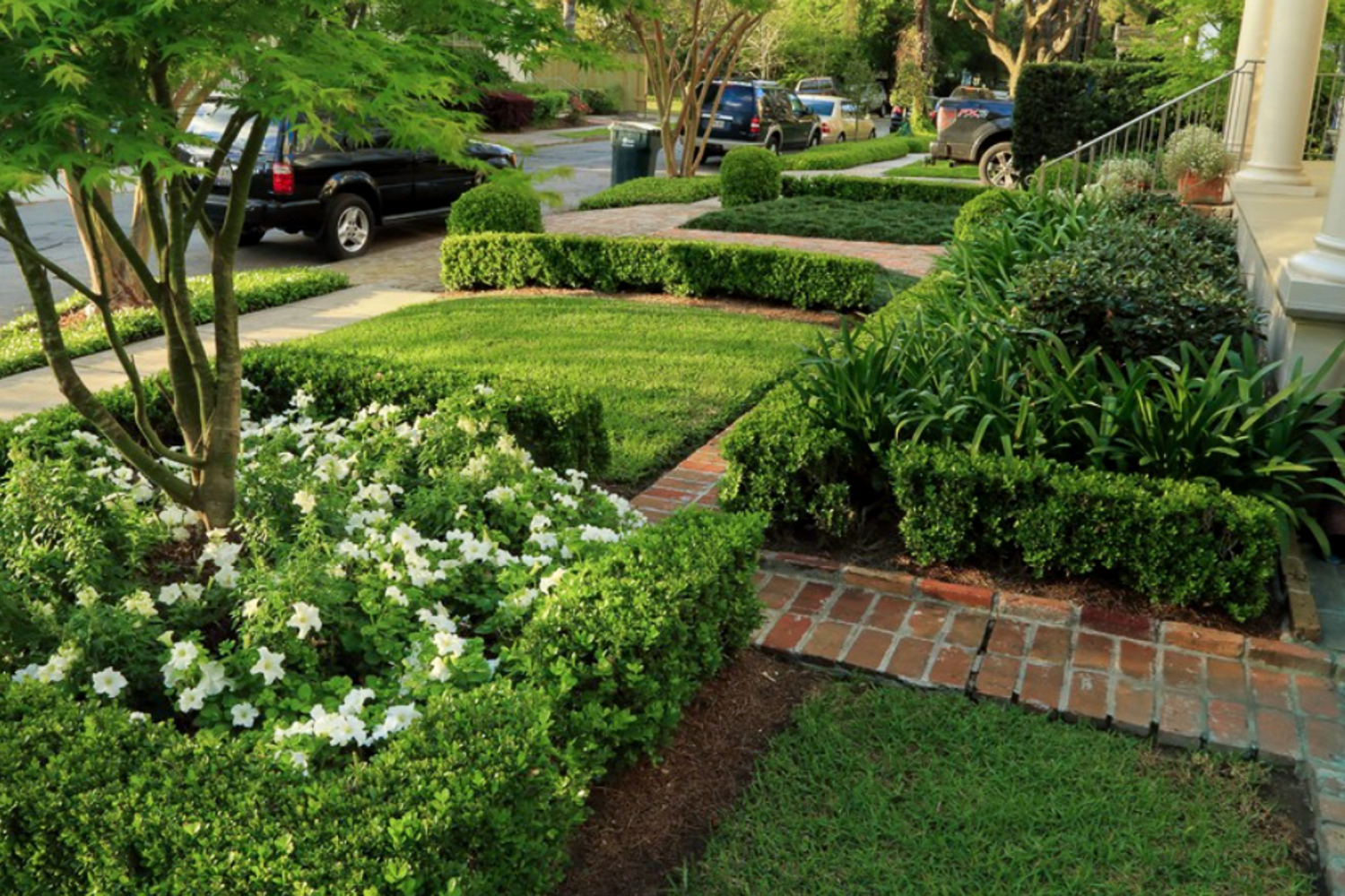 Formal courtyard landscape design with brick paving, clipped boxwood, central planting bed, and symmetrical garden paths.