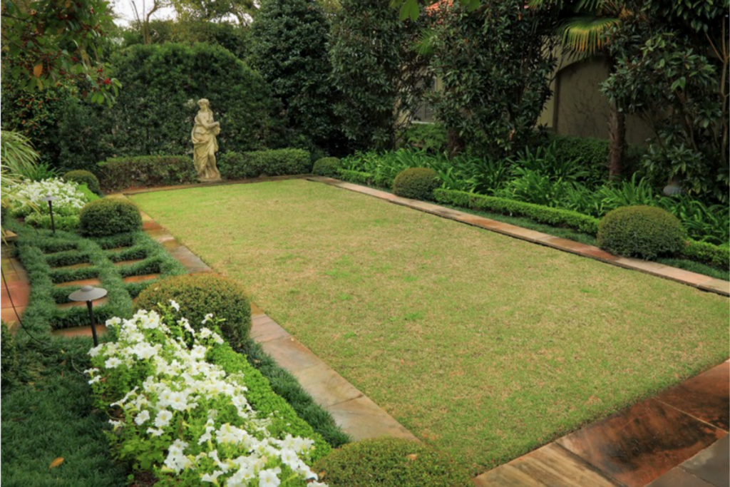 Formal landscape design with classical statue, white flowers, clipped shrubs, lawn, and layered evergreen planting.