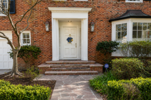 Flagstone entry walk leading to the front steps of the Nashville Avenue Garden in Uptown New Orleans, bordered by evergreen planting and brick architecture.