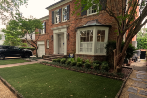 Traditional brick home framed by lawn panels, brick-edged planting, flagstone paths, and mature trees at Nashville Avenue Garden in Uptown New Orleans.