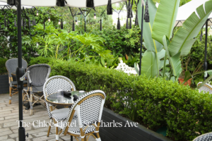 Outdoor dining terrace at The Chloe Hotel, surrounded by clipped hedges, tropical planting, and mature greenery.