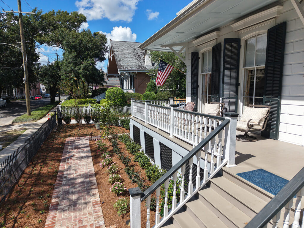 View from the front porch of a historic New Orleans home overlooking brick walkways and newly planted garden beds.