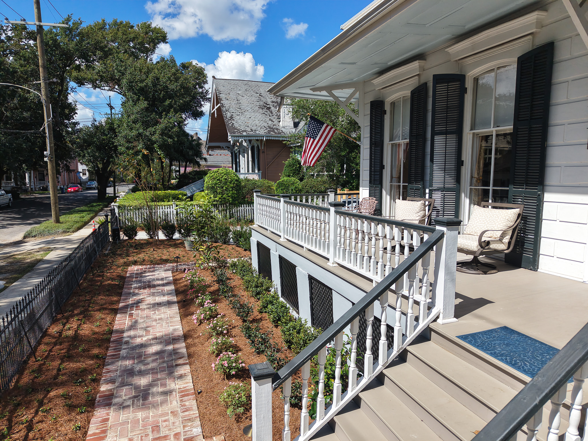 View from the front porch of a historic New Orleans home overlooking brick walkways and newly planted garden beds.