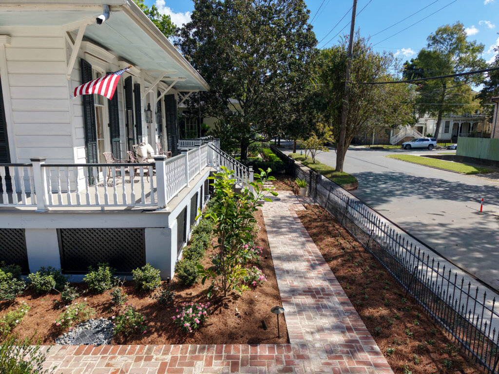 Aerial view of brick walkways and front-garden planting beside a historic New Orleans home.