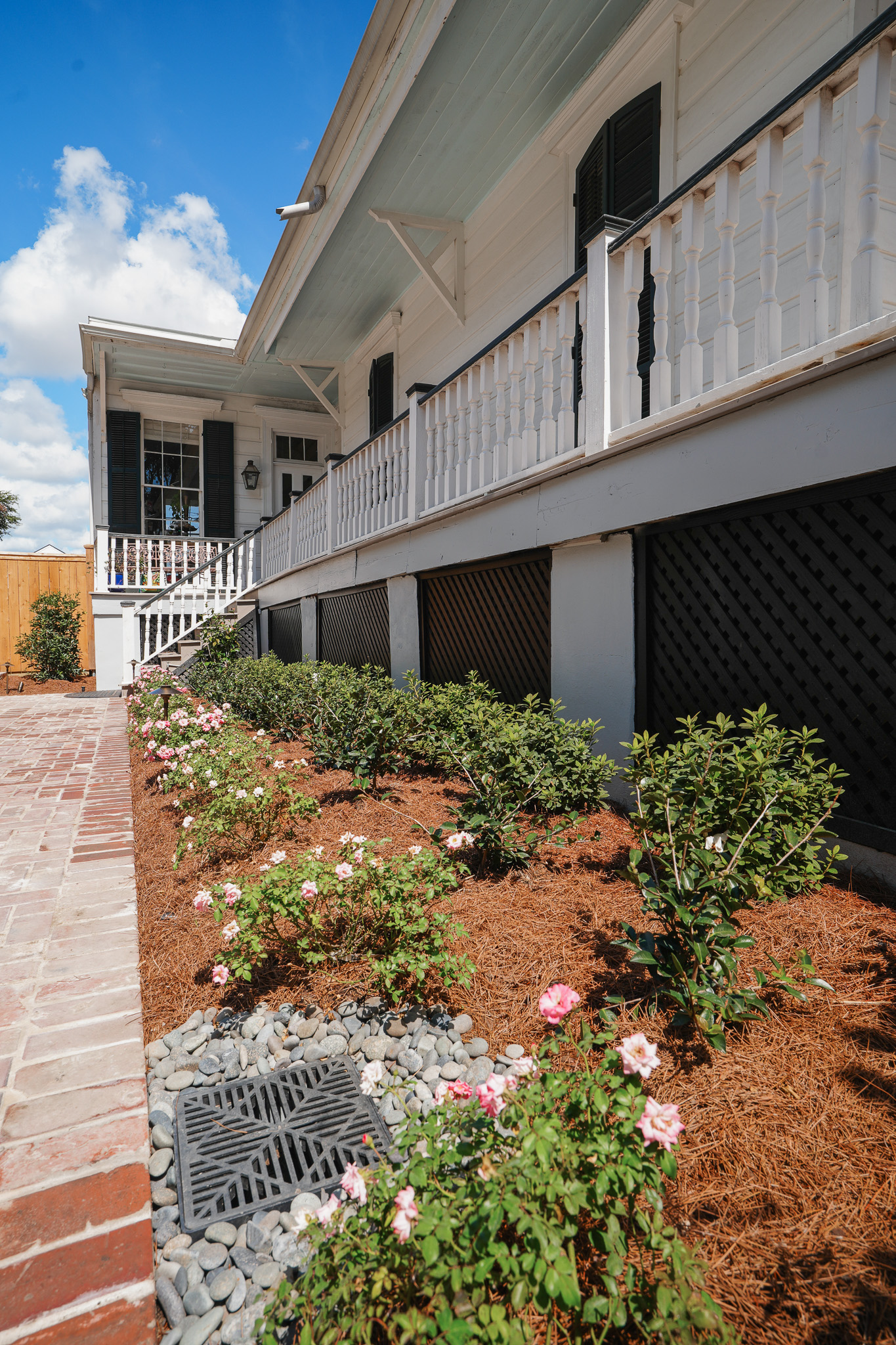 Raised front porch with white balustrade, brick paving, flowering shrubs, and foundation planting.