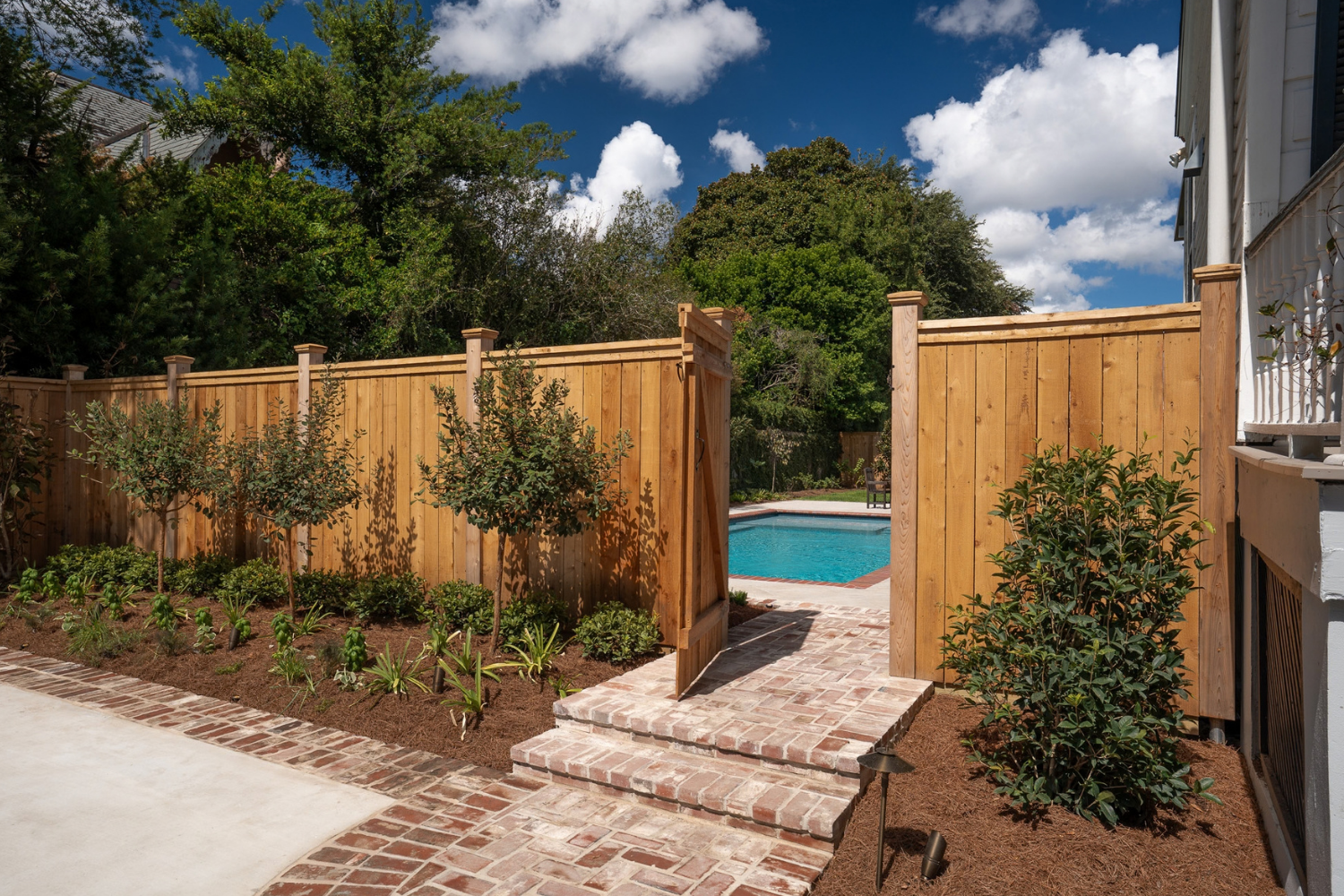 Wood garden gate and brick steps leading to a pool garden at a New Orleans home.