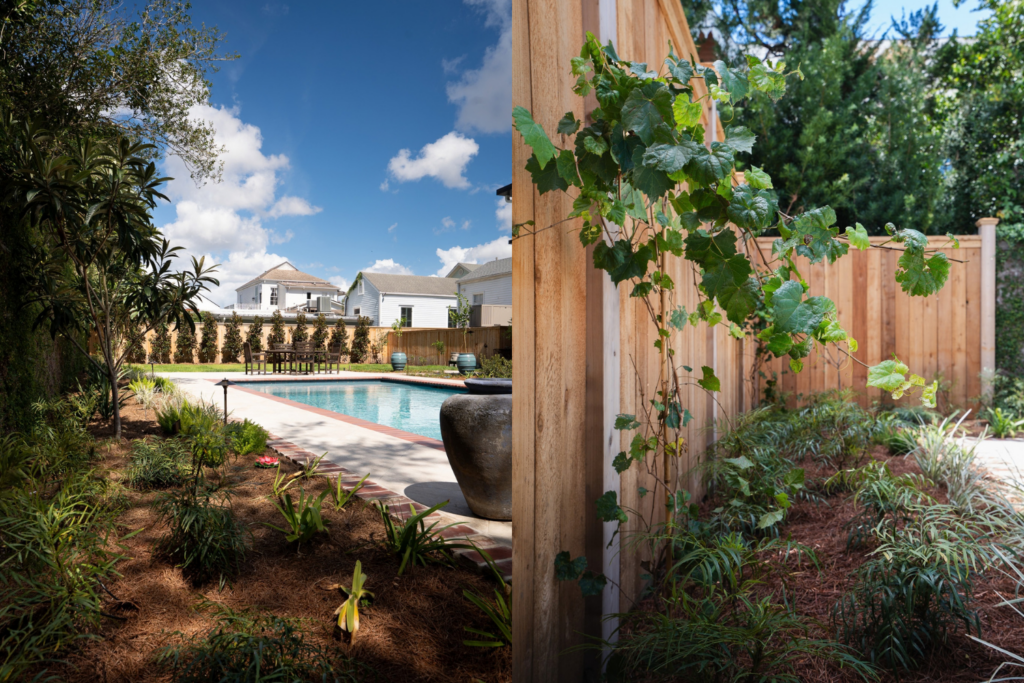 Pool garden with brick-edged paving, layered planting, and a wood privacy fence in New Orleans.
